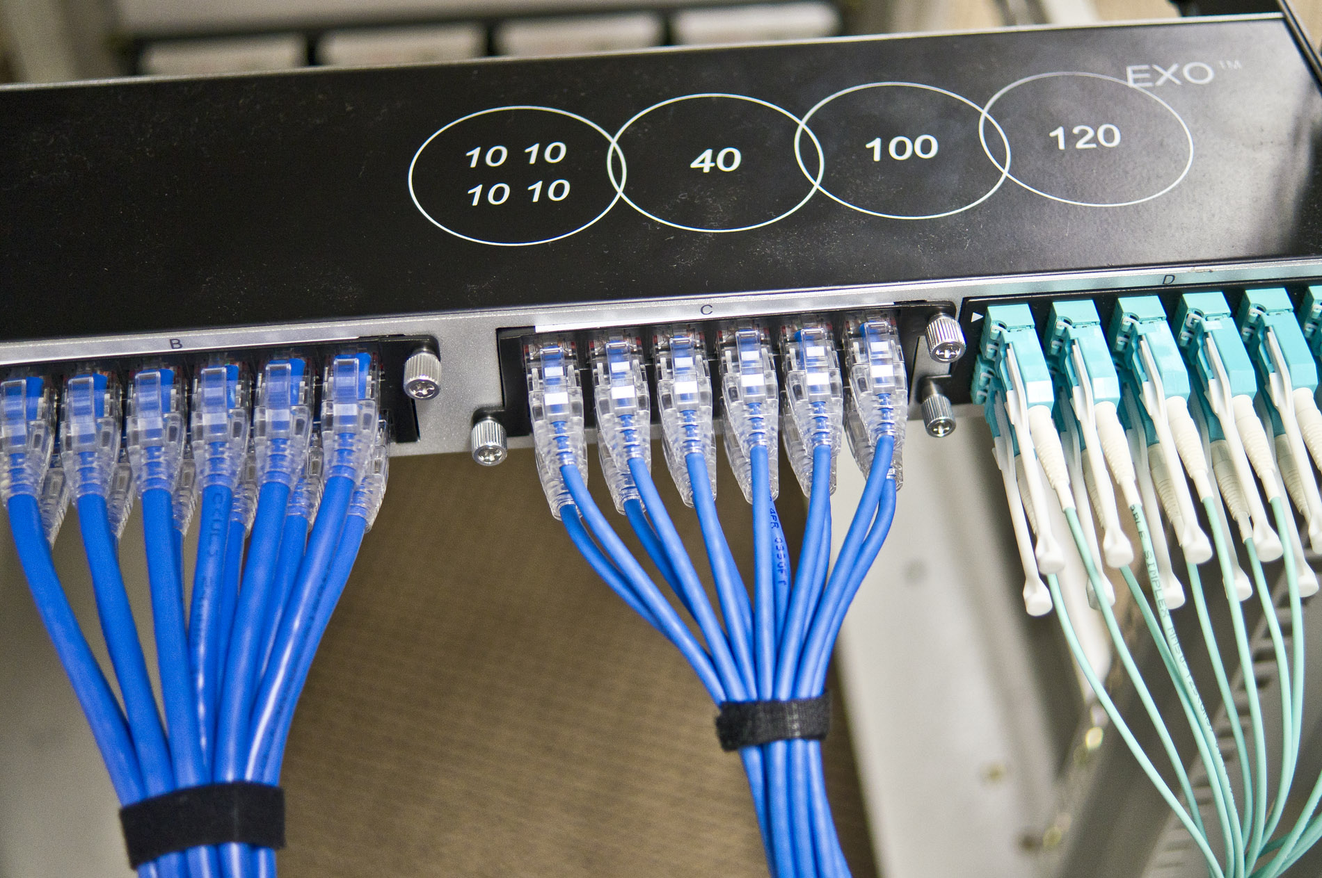 Quality assurance technician using handheld fiber optic test equipment showing PASS result, with color-coded cable coils in manufacturing facility background